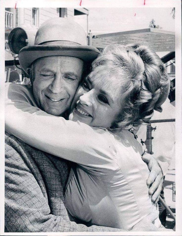 an old black and white photo of a man hugging a woman's head while she is wearing a hat