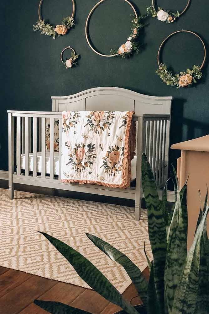 a white crib in a green room with flowers on the wall and plants hanging above it