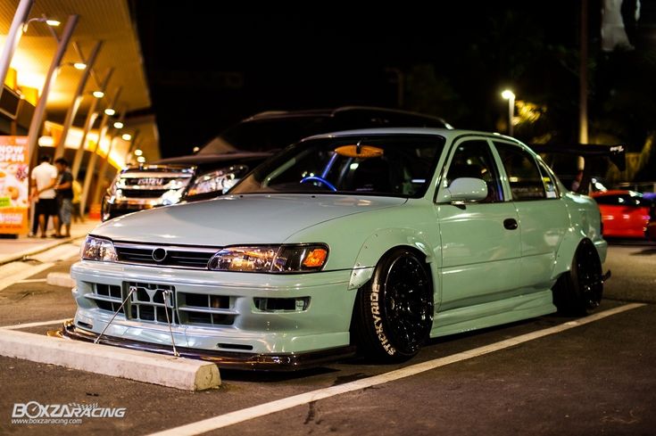 a green car parked in the middle of a parking lot next to other cars at night