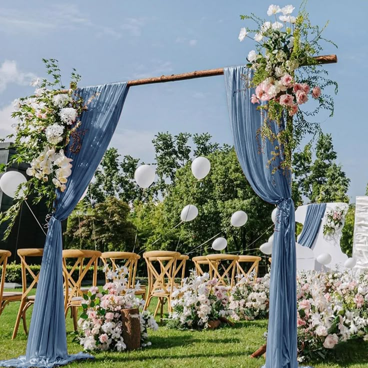 an outdoor wedding setup with blue drapes and white flowers on the grass, balloons in the air