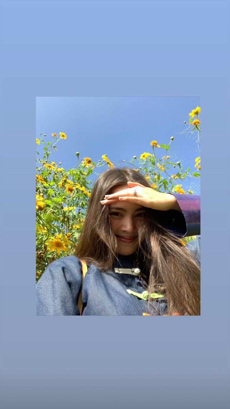 a woman is holding her hair in front of the sunflowers and blue sky