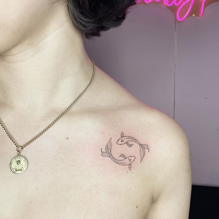 a woman's chest with a tattoo on it and a pink neon sign in the background