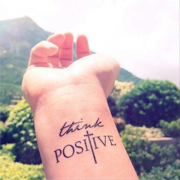 someone is holding up their wrist tattoo with the words think positive on it in cursive writing