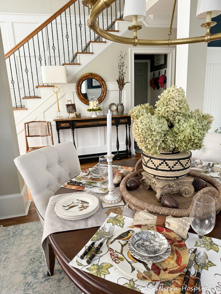 a dining room table is set with place settings and flowers in a basket on the centerpiece