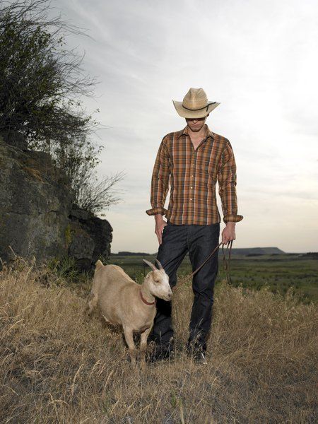 a man standing next to a sheep on top of a dry grass field