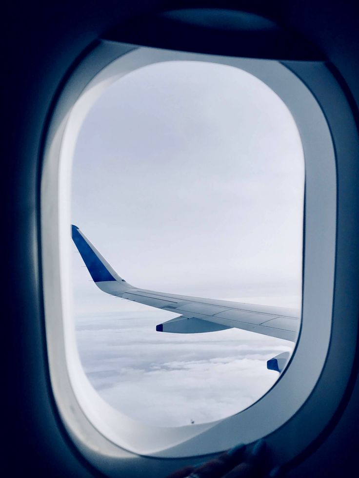 an airplane window looking out at the clouds and sky from inside another plane's wing