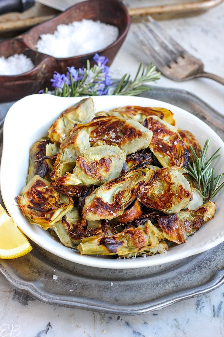 a white bowl filled with cooked artichokes on top of a table