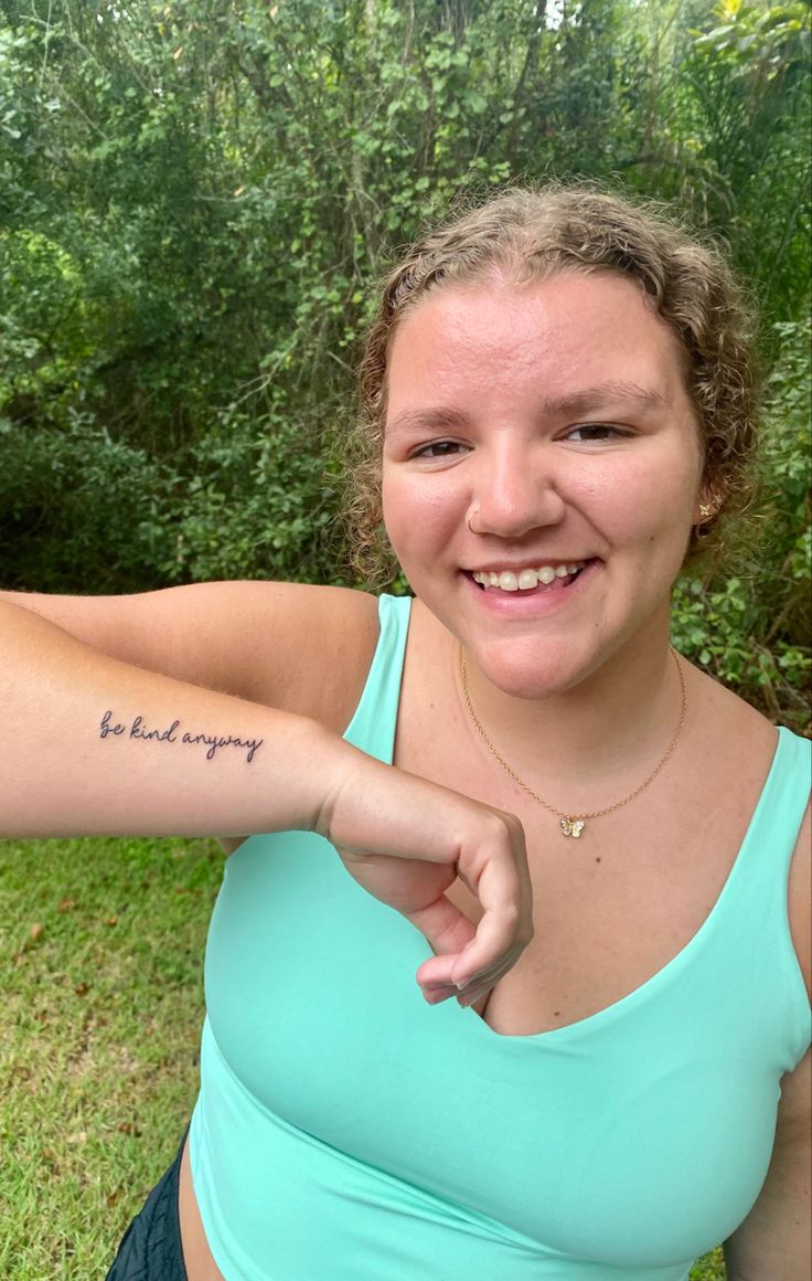 a woman with a tattoo on her arm pointing to the side and smiling at the camera