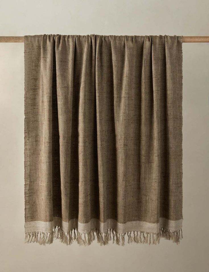 a tan curtain hanging from a wooden rod with fringes on the top and bottom