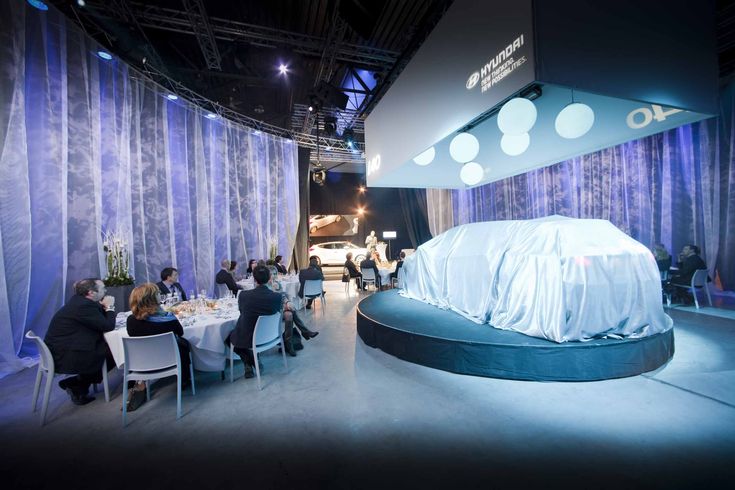 people sitting at tables in front of a car covered with a white cloth on it