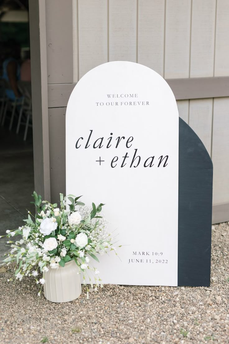 a welcome sign with flowers on the ground in front of a building that says claire + eiban