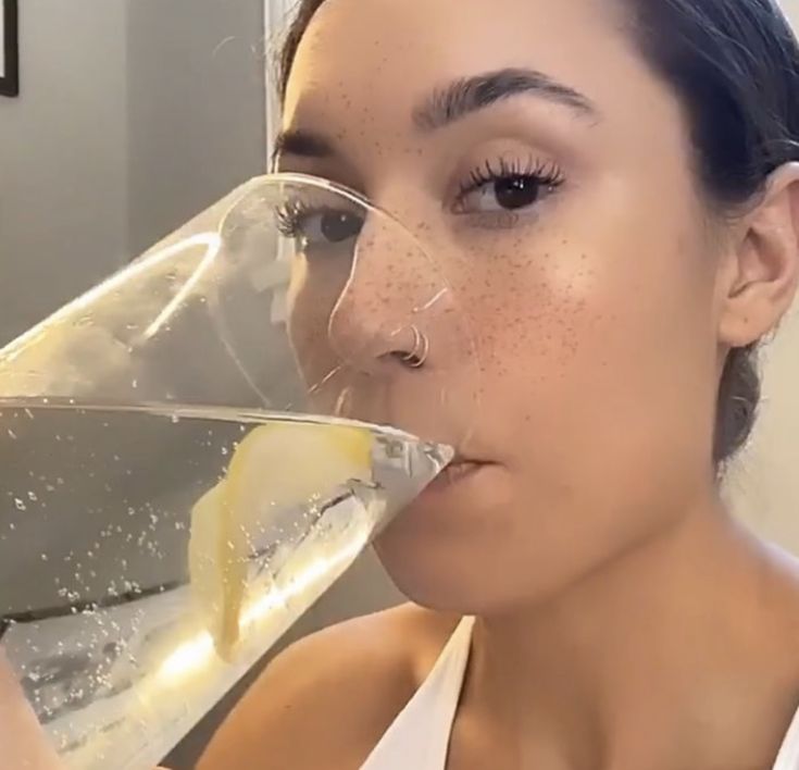 a woman drinking from a wine glass in front of her face and wearing a white tank top