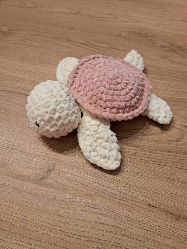 a crocheted stuffed turtle laying on top of a wooden floor next to a pink and white hat