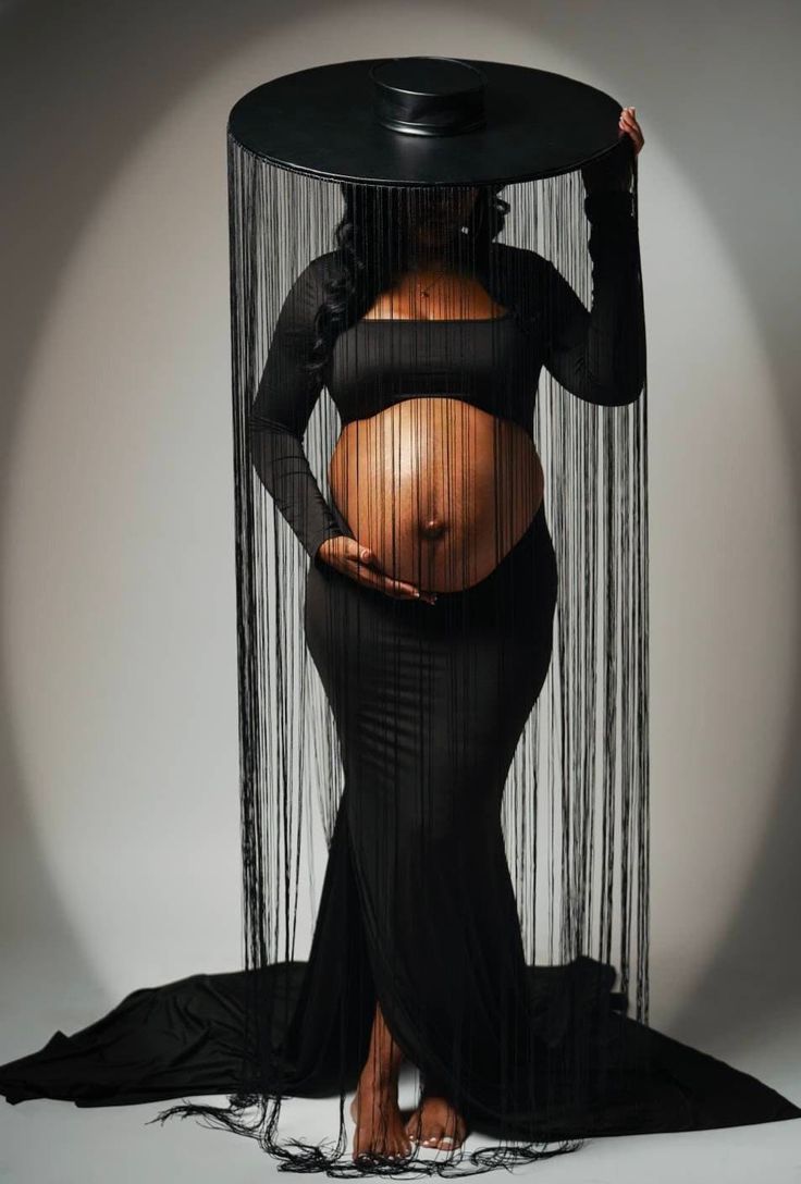 a pregnant woman is standing in front of a sheer curtain with her hands on her hips