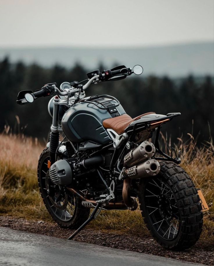 the motorcycle is parked on the side of the road near some tall grass and trees