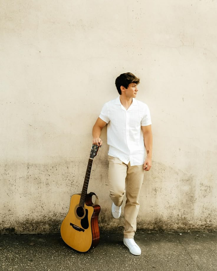 a man standing next to a wall with a guitar in front of him and leaning against the wall