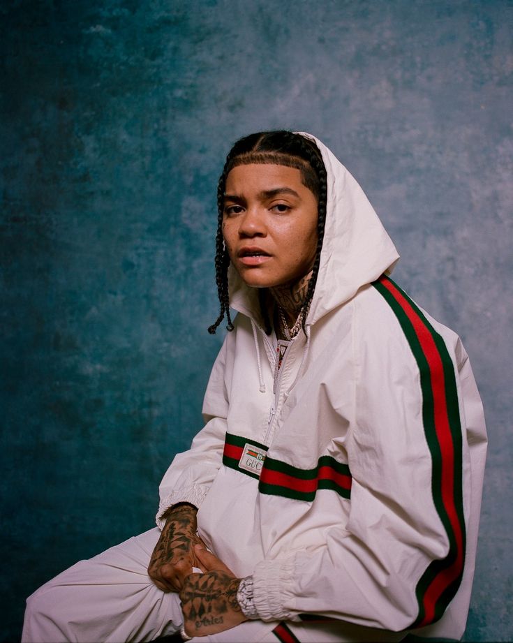 a man with dreadlocks sitting in front of a blue wall wearing a white hoodie