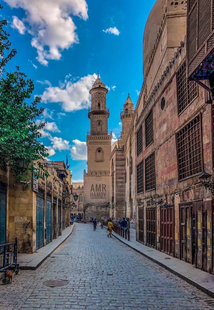 an old city street with people walking on the sidewalks and buildings in the background, under a blue sky with white clouds