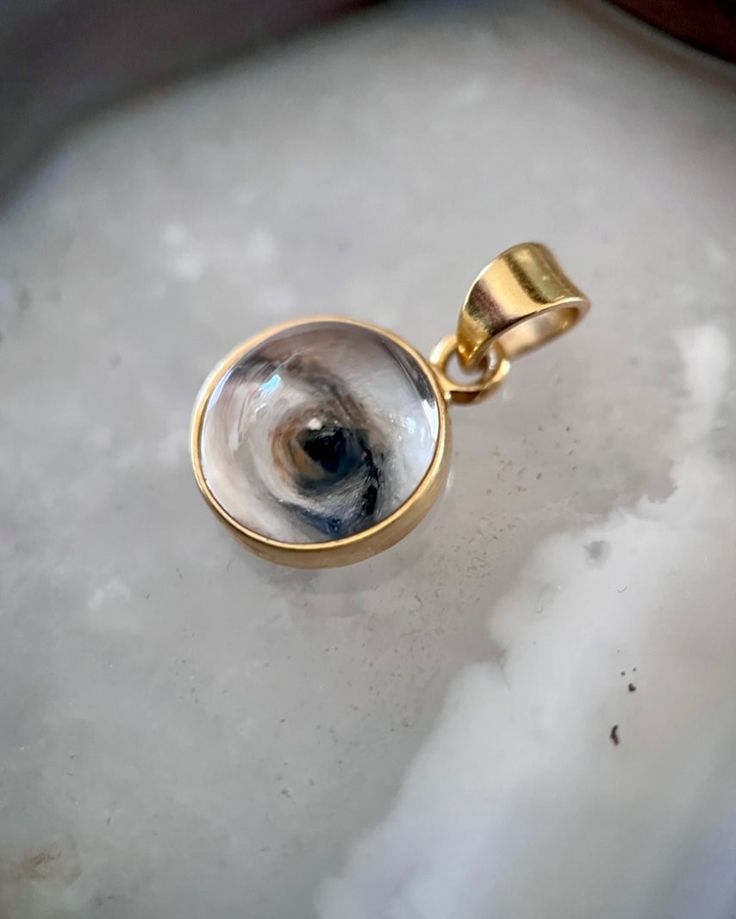 Lover's Eye pendant with an oil painting encased in gold plate over sterling with a quartz crystal cabochon which gives a magical magnifying effect, measuring 1/2" in diameter; 18" 16k gold over brass chain included. THE HISTORY: Lover's Eyes were a jewelry trend c.1785-1830 of brooches set with tiny watercolor portraits on ivory. Since they were cropped to eyes, they were in many ways more direct and intimate than traditional miniature portraits; but also because they were just eyes, they were Round Pendant Jewelry With Rotating Bezel Gift, Rotating Bezel Round Pendant Jewelry As A Gift, Amulet Style Round Pendant Jewelry For Memorial, Gift Jewelry Medallion With Rotating Bezel, Medallion Jewelry With Rotating Bezel For Gifts, Collectible Gold Birthstone Jewelry, Gold Spiritual Jewelry For Keepsake, Keepsake Jewelry Round Pendant With Natural Inclusions, Memorial Amulet Jewelry With Round Pendant