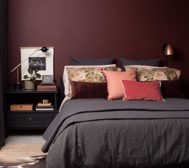 a bedroom with dark purple walls and black bedding, red pillows, and white headboard