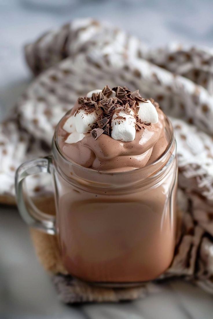 a glass jar filled with hot chocolate and marshmallows on top of a table