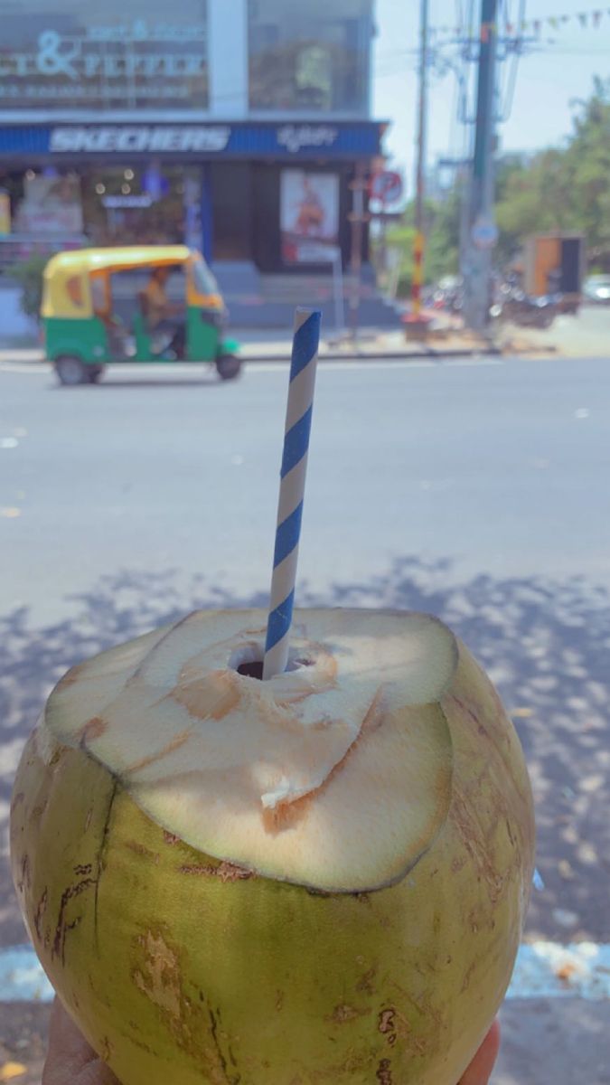 a person holding up a coconut drink with a blue and white straw in it's mouth