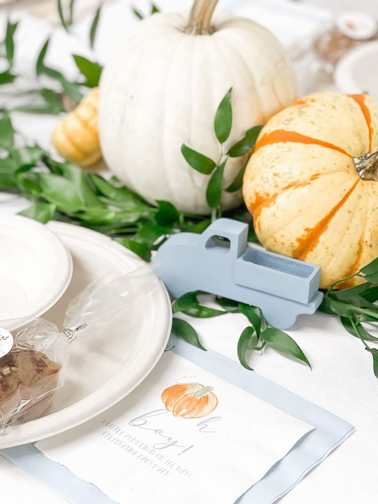 a table topped with white plates covered in pumpkins and greenery on top of it