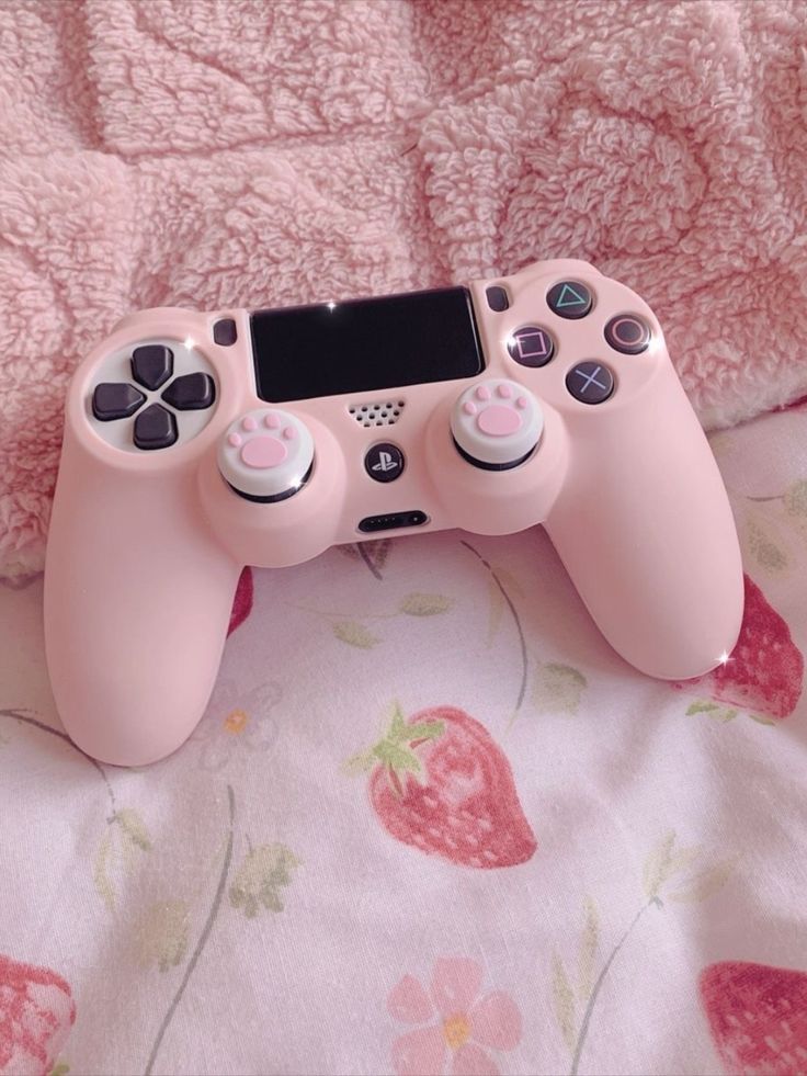 a pink video game controller sitting on top of a bed next to a pink blanket