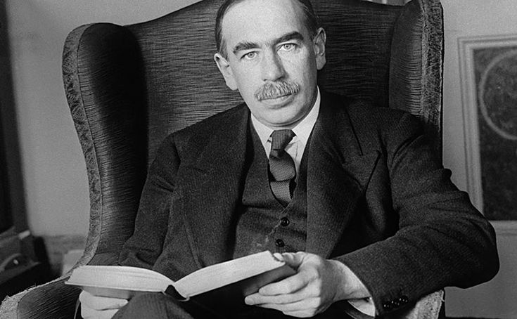 a man sitting in a chair holding a book and looking at the camera while reading it