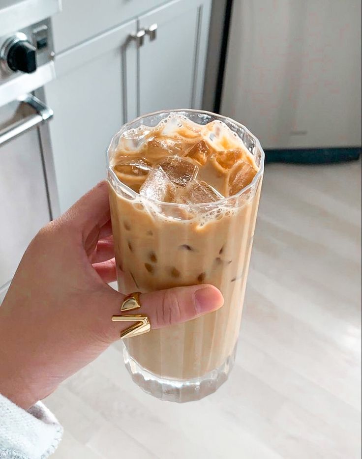 a person holding up a drink with ice and caramel on it in front of an oven