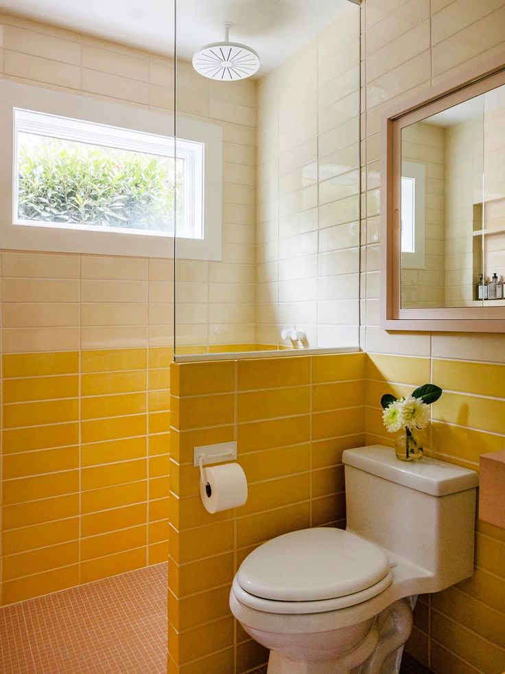 a white toilet sitting next to a sink in a bathroom under a mirror and a window