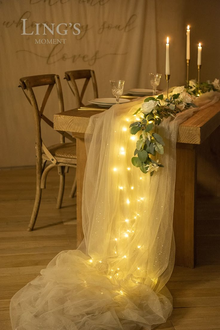 the table is set with candles and flowers on it, along with sheer tulle