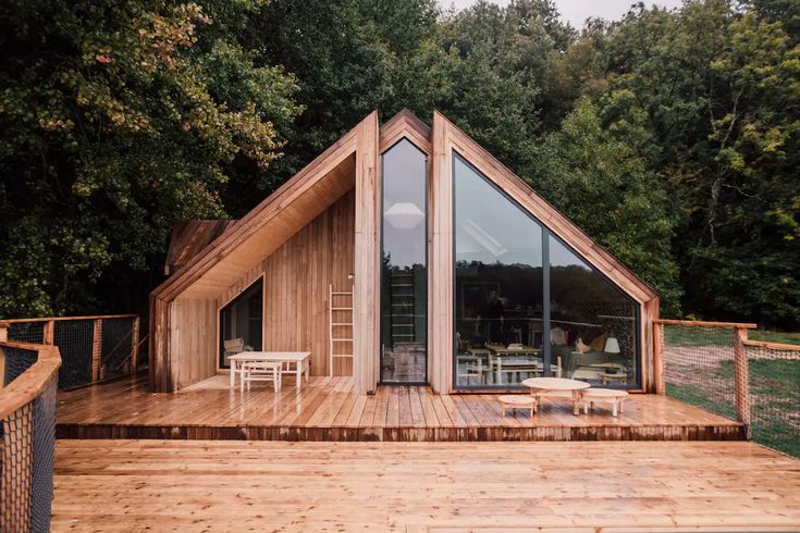 a wooden deck with chairs on it next to a small house in the middle of trees