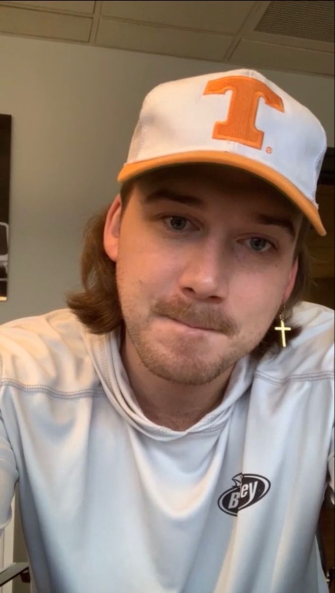 a man with long hair wearing a white shirt and orange hat looking at the camera