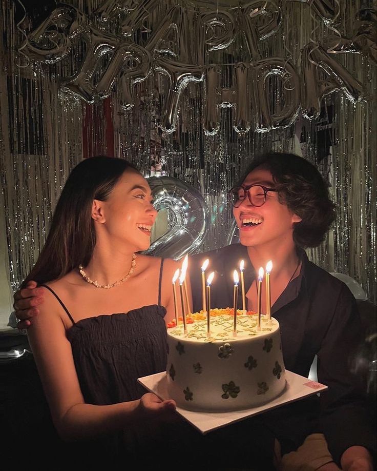 two women sitting next to each other in front of a cake with candles on it