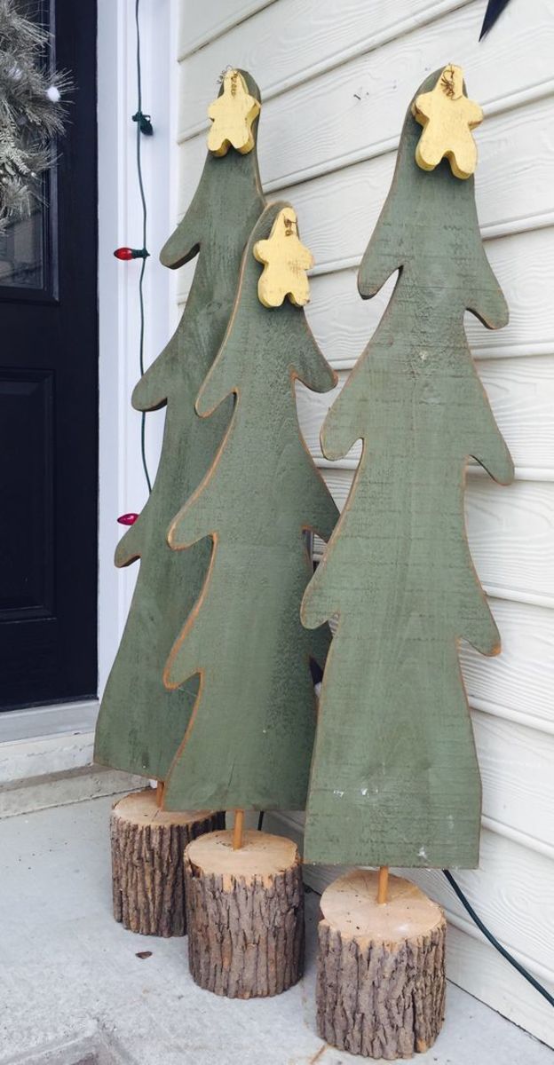 three wooden christmas trees sitting next to each other on top of a tree stump in front of a house