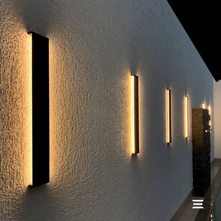 three lights are on the side of a white wall next to a pool and water feature