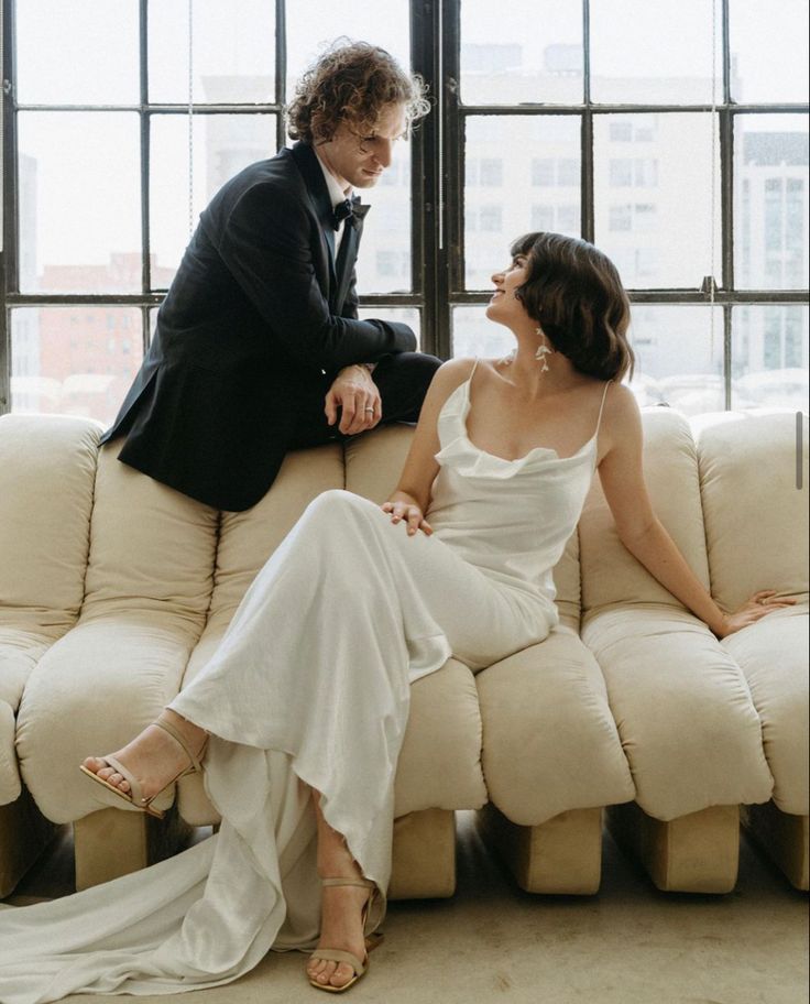 a bride and groom sitting on a couch looking at each other