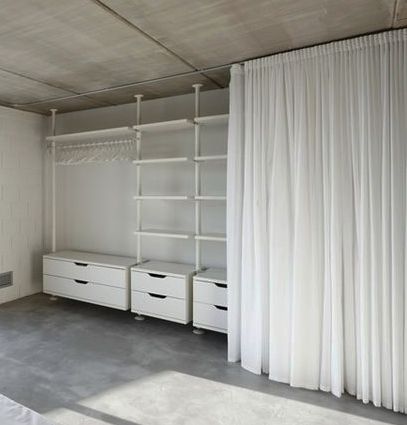 an empty bedroom with white curtains and drawers