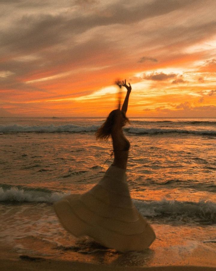 a woman is dancing on the beach at sunset