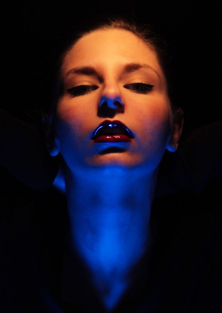 a woman with her eyes closed in the dark, wearing blue light makeup and black hair