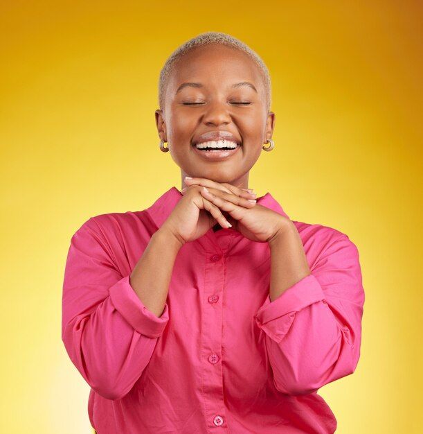 a woman in pink shirt smiling and holding her hands to her chest while standing against a yellow background