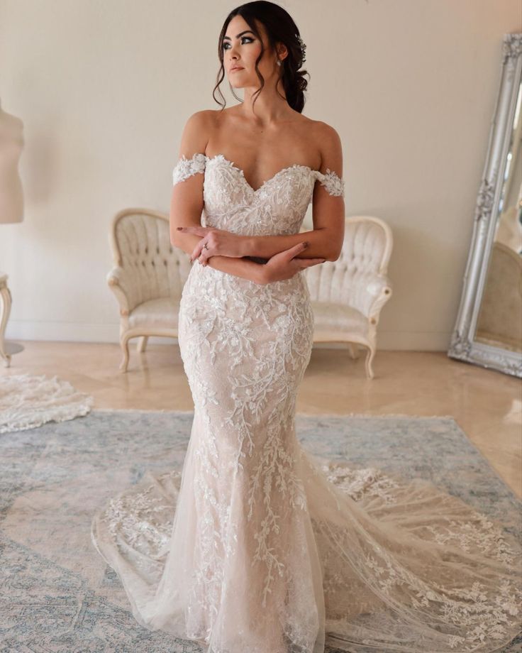 a woman in a wedding dress standing on a rug with her arms crossed and looking off to the side