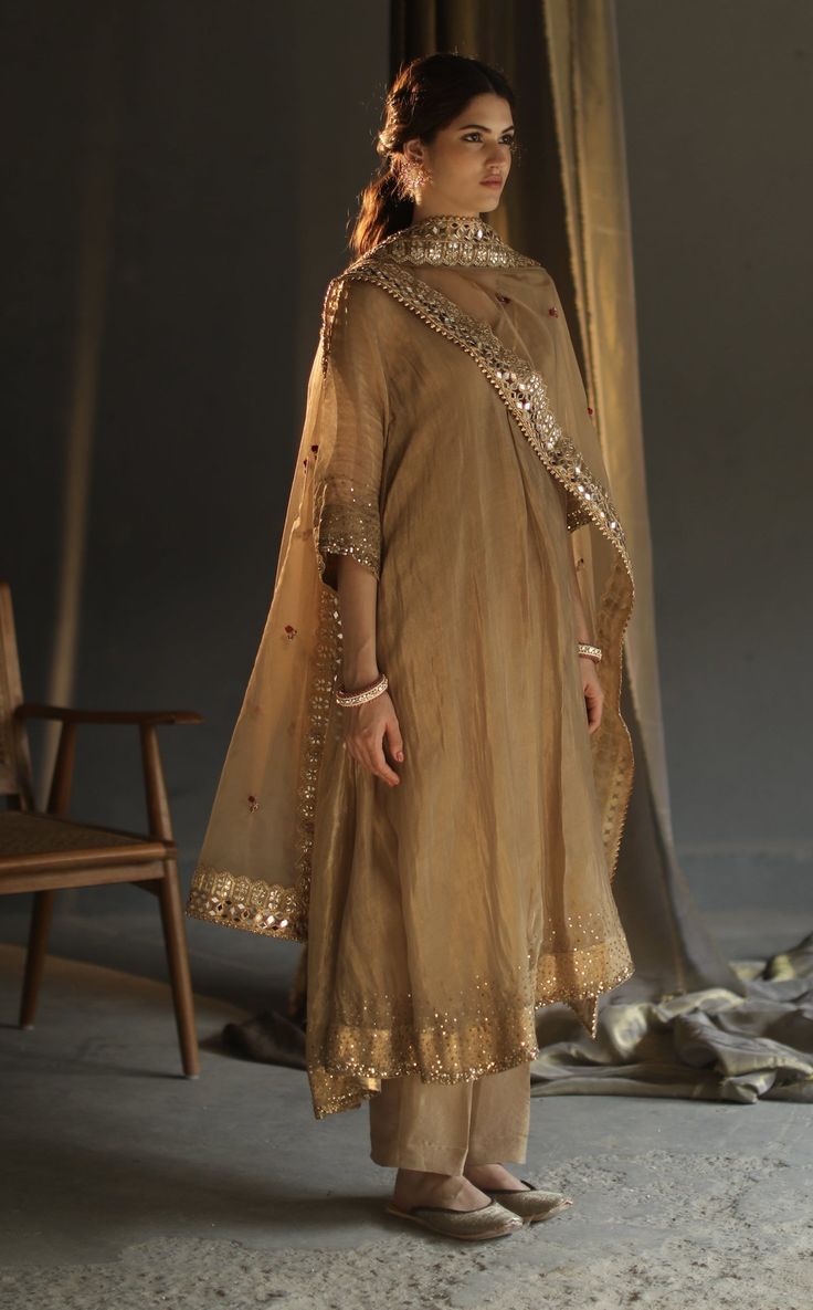 Editor's Note Featuring A-Line Asymmetrical Kurta Set with Mirror Work, Hand Embroidered Floral Bootis, Hand Sequinned Embroidery Color: Beige Fabric: Chanderi Zari - Kurta, Organza - Dupatta, Chanderi Zari - Pants, Mulmul Slip Care: Dry Clean Only About the Designer Begum celebrates heritage and rare craftsmanship on traditional silhouettes. Our pieces can be best defined as summer personified with artisanal hand embroideries, hand appliqués and ancient techniques revived in the present day han Luxury Unstitched Organza Kurta, Luxury Katan Silk Kurta For Eid, Luxury Kurta With Zari Weaving For Festivals, Luxury Kurta With Zari Work And Stand Collar, Luxury Mirror Work Salwar Kameez Maxi Length, Luxury Nida Salwar Kameez With Mirror Work, Luxury Naqshi Kurta For Formal Occasions, Luxury Chanderi Traditional Wear For Diwali, Luxury Naqshi Kurta For Party