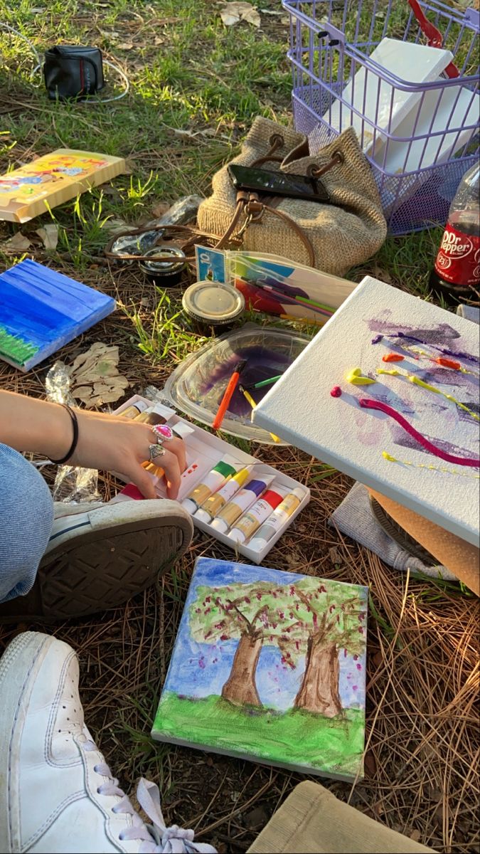 a person sitting on the ground with some art supplies in front of her and painting