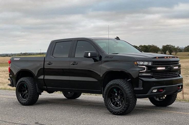 a black truck is parked on the side of the road in front of a field