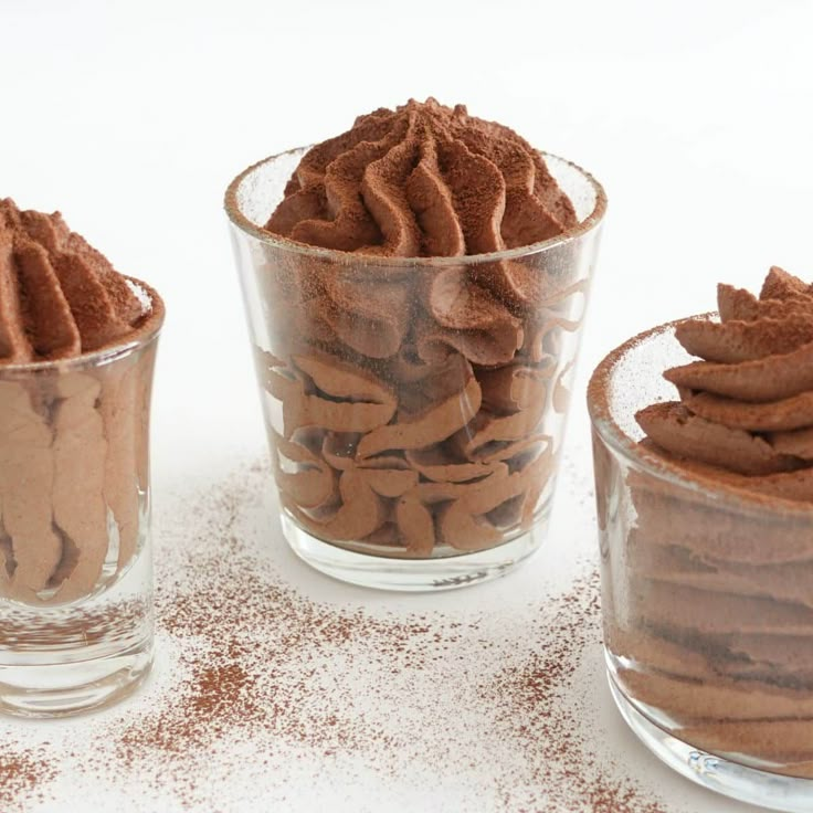 three glass bowls filled with chocolate desserts on top of a white countertop next to each other