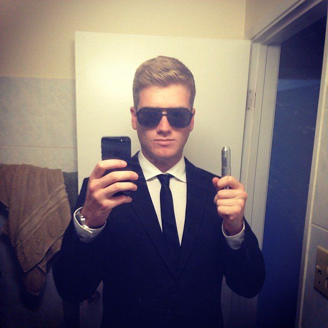 a man in a suit taking a selfie with his cell phone while wearing sunglasses