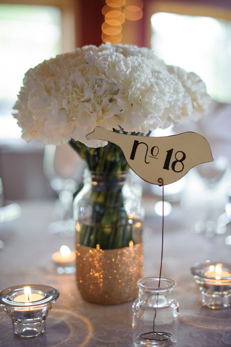 a vase with white flowers and candles on a table in front of a number sign