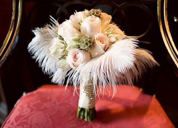 a bridal bouquet sitting on top of a red cloth covered chair next to a gold framed mirror